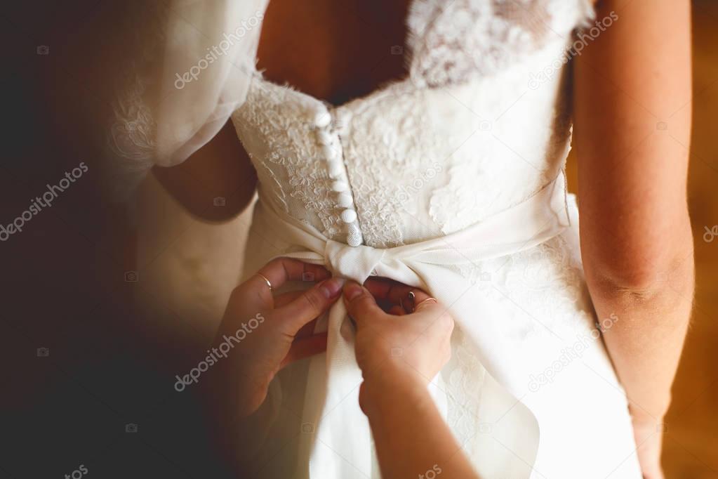 Hands put on a bow on delicate bride's waist 