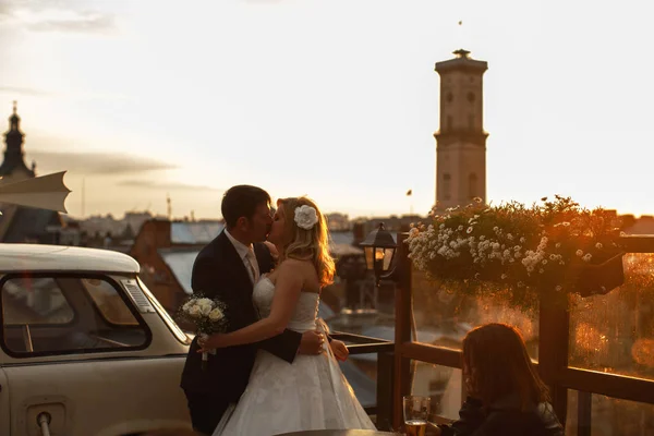 Ein Hochzeitspaar küsst zärtlich auf dem Dach stehend vor einem — Stockfoto