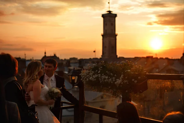Die Sonne geht über einer alten Stadt unter, während Braut und Bräutigam stehen — Stockfoto