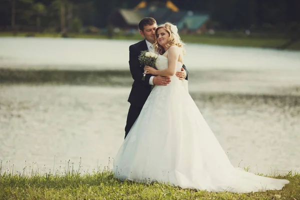 Наречений і наречений обіймають один одного стоячи на березі озера — стокове фото