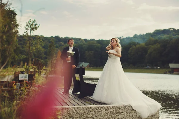 La novia está detrás de un lago mientras el novio la admira — Foto de Stock