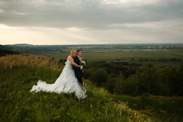 Noiva abraços noivo por trás de pé na colina — Fotografia de Stock