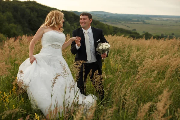 Casado casal sorri andando em uma grama alta — Fotografia de Stock