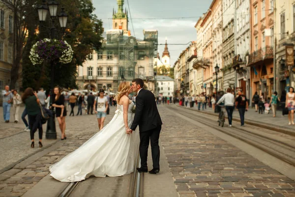 Bräutigam küsst eine charmante Braut, während der Wind ihr Kleid entlang weht — Stockfoto