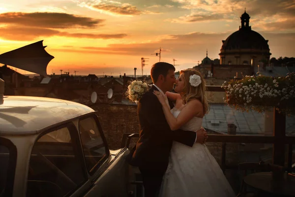 Ein Hochzeitspaar küsst unter dem Abendhimmel auf dem Dach — Stockfoto