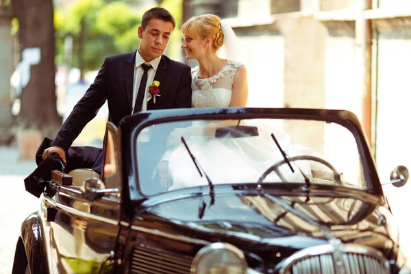 Ein Hochzeitspaar sitzt auf einem schwarzen Retro-Cabrio — Stockfoto