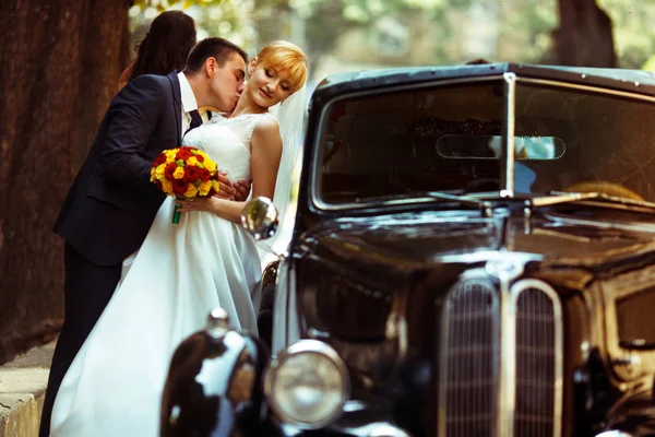 Prometido besa el cuello de la novia de pie detrás de un coche negro retro —  Fotos de Stock