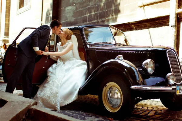 Groom embrasse une mariée alors qu'elle est assise dans une vieille voiture — Photo