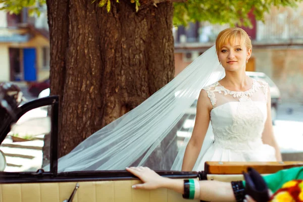 Een uitzicht op een prachtige blonde bruid uit een retro auto — Stockfoto