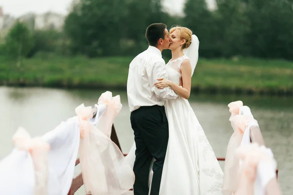 Um casal de casamento beija ternamente em pé em uma ponte decorada — Fotografia de Stock