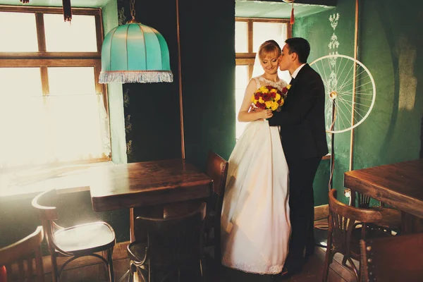 Groom kisses bride in a cheek while they stand in an old restaur — Stock Photo, Image