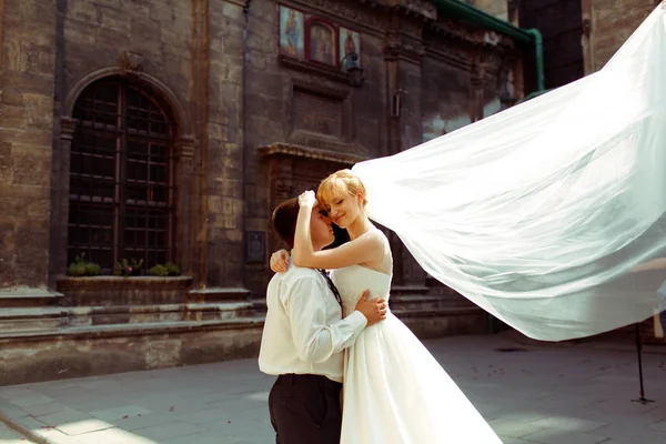 Bride leans to groom's head tenderly while wind blows away her v — Stock Photo, Image