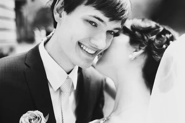 Молодой и счастливый жених улыбается, а невеста целует его в ухо. — стоковое фото