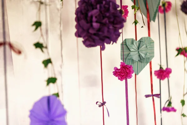 Green paper hearts and violet paper flowers hang on pink ribbons — Stock Photo, Image