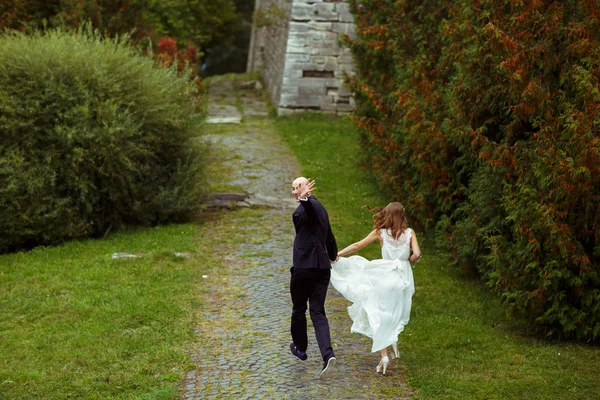 Bräutigam winkt mit der Hand, während er mit der Braut entlang des Schulterklopfens läuft — Stockfoto