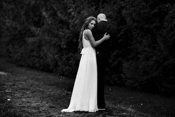 Удивительная невеста обнимает жениха, оглядываясь через плечо — стоковое фото