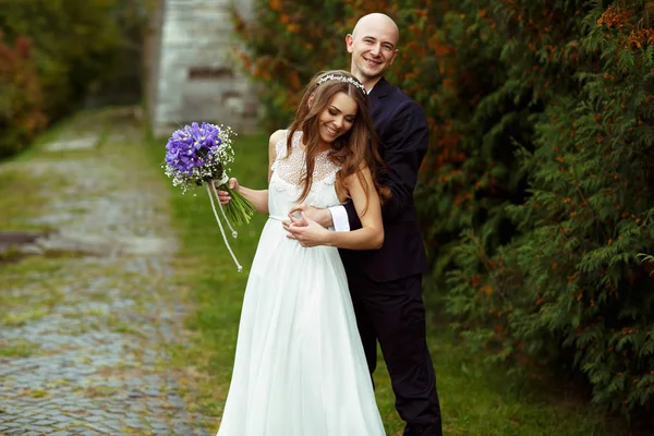 Braut lächelt, während ein Bräutigam sie zärtlich von hinten umarmt — Stockfoto