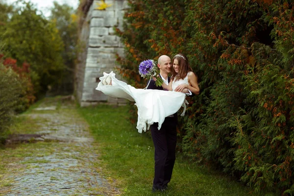Bruidegom loopt met een bruid op zijn armen langs het park — Stockfoto