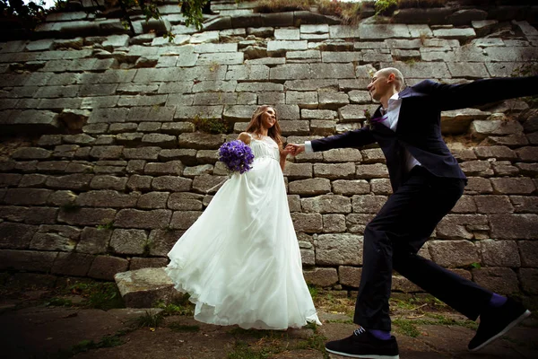 Groom runs to a bride while she waits for him behind a stone wal — Stock Photo, Image