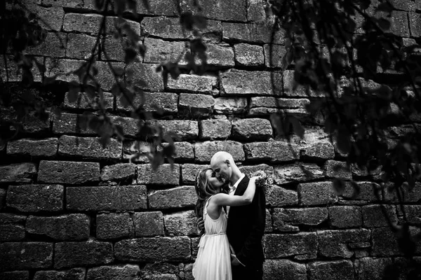 Bride hugs groom tenderly standing alone behind an old castle — Stock Photo, Image