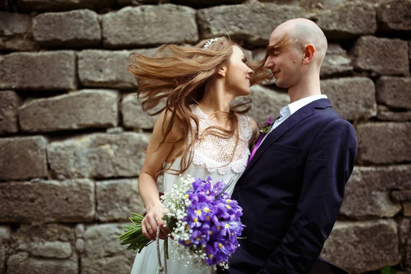 Braut berührt das Gesicht des Bräutigams mit den Haaren, die hinter einem Stein stehen — Stockfoto
