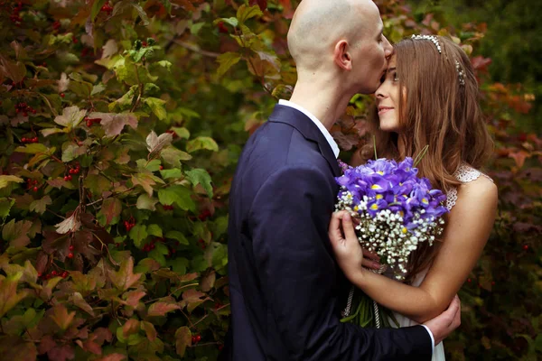 Noiva segurar um buquê de casamento atrás de seu peito, enquanto noivo beijos — Fotografia de Stock