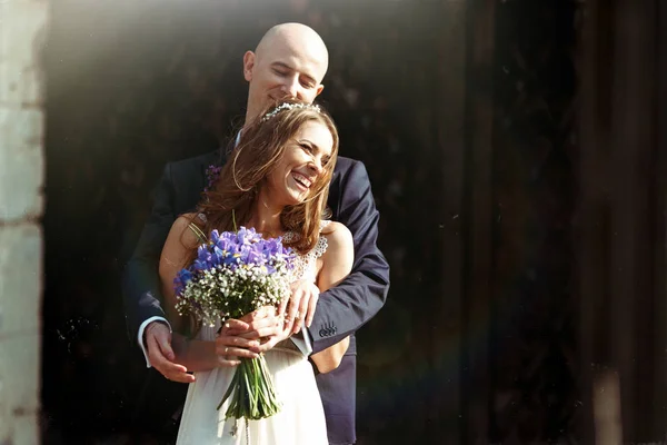 Braut lächelt funkelnd, während Bräutigam sie von hinten umarmt — Stockfoto