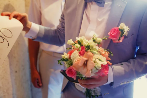 Bruidegom in licht blauw pak houdt een roze bruiloft bouqet — Stockfoto