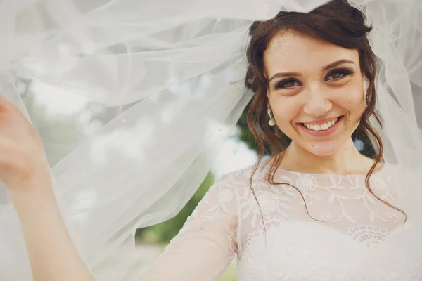 Increíble novia morena sonríe amplia sosteniendo su velo — Foto de Stock