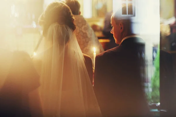 A view from behind on groom and bride praying with candles in th