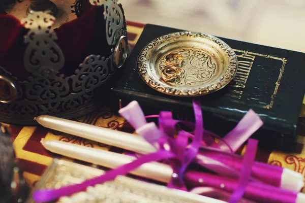 Anillos de boda se encuentran en un plato de oro detrás de la corona y velas en —  Fotos de Stock