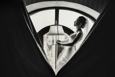 Gelin bir vintage lamba ayakta büyük bir pencere önünde tutar.