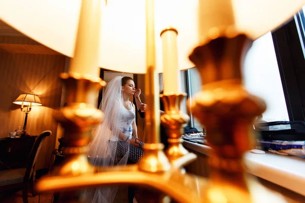 Una mirada a través de una lámpara en una novia mientras ella hace un maquillaje —  Fotos de Stock
