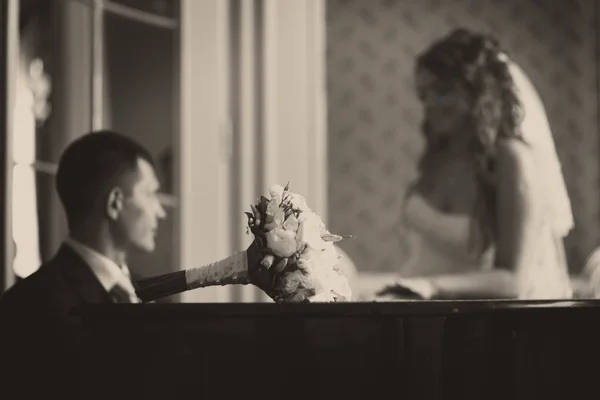 Bruiloft boeket ligt op de piano terwijl bruidegom voor een bruid speelt — Stockfoto