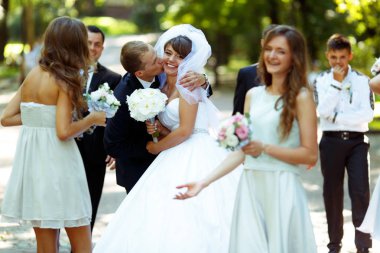 Groom kisses bride's cheek and hugs her while they walk with fri