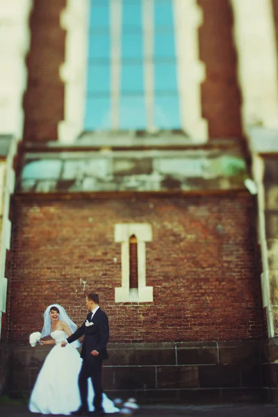 Novia y novio de pie bajo una gran ventana de una antigua catedral — Foto de Stock