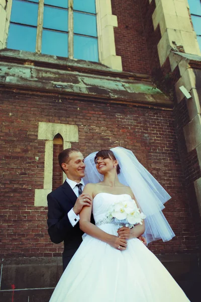 Novia y novio sonríen mientras posan detrás de una vieja catedral —  Fotos de Stock