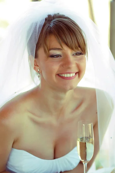 Impresionante novia sonríe sosteniendo una copa con champán en su brazo —  Fotos de Stock