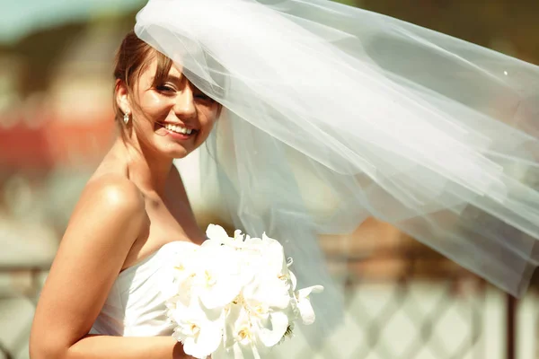 Die Braut lächelt mit einem weißen Strauß im Arm, während der Wind bläst — Stockfoto