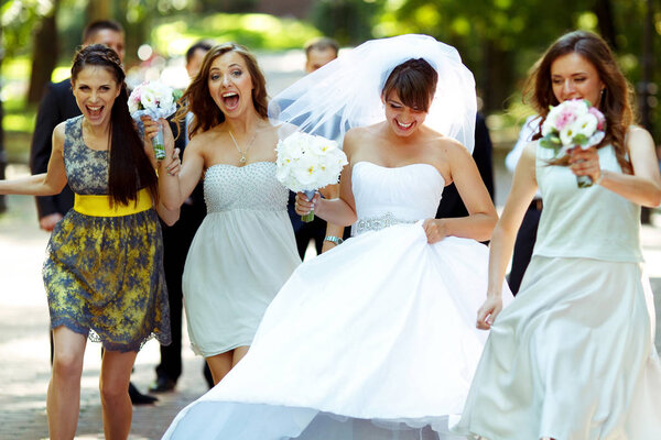 Happy bride and bridesmaids walk along the path in the park 