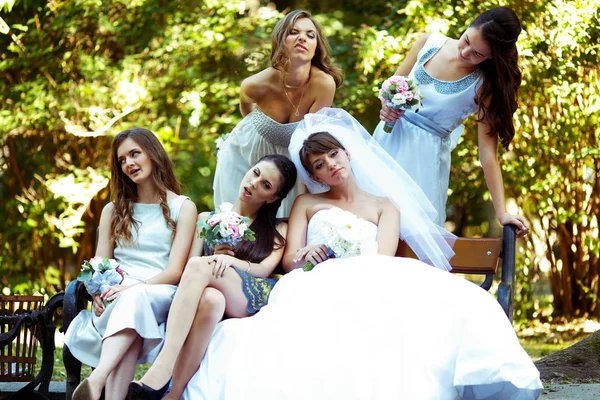 Nevěsta a družičky grimasa sedí na lavičce v parku — Stock fotografie