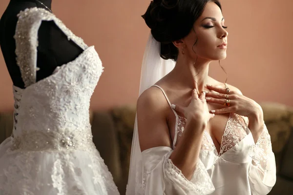 La novia encantadora se encuentra cerca del vestido de novia en la habitación —  Fotos de Stock