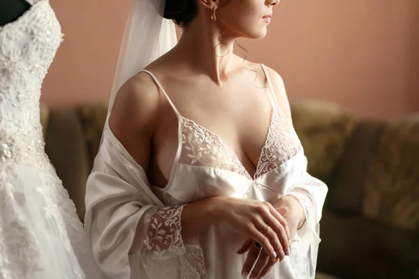 Die charmante Braut steht neben dem Brautkleid im Zimmer — Stockfoto