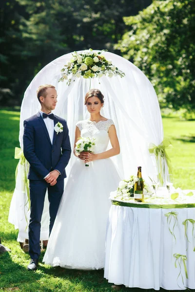 Beau couple de mariage se tient derrière un autel de mariage blanc dans — Photo
