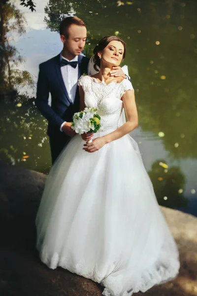 Sposo tocca una sposa tenera in piedi sulla grande pietra dietro un — Foto Stock