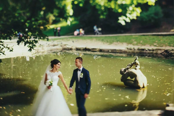 Наречений і наречений гуляють уздовж берега паркового озера — стокове фото