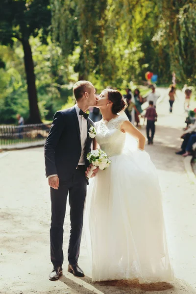 Sposa e sposo bacio in piedi nel parco pieno di gente — Foto Stock