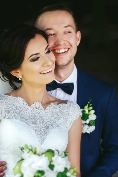 Groom sorri segurando uma noiva delicada em seus braços — Fotografia de Stock