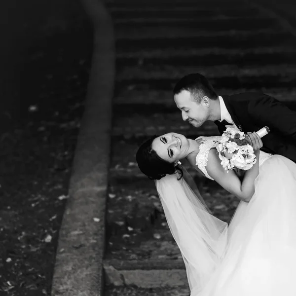 Sposo piega sposa sopra in piedi sulle orme del parco coperto wi — Foto Stock