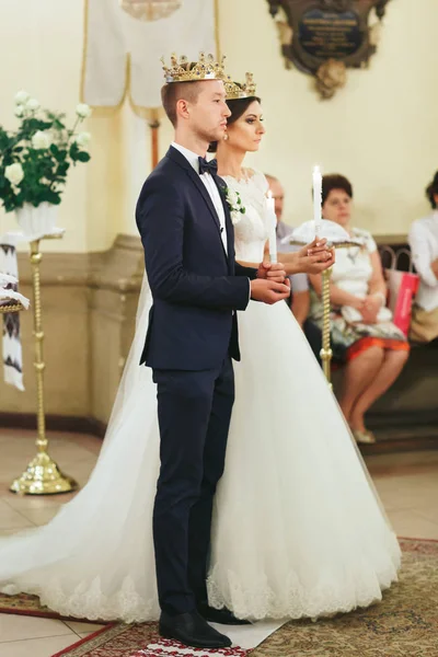 Noiva e noivo segurar velas de pé nas coroas em uma igreja — Fotografia de Stock
